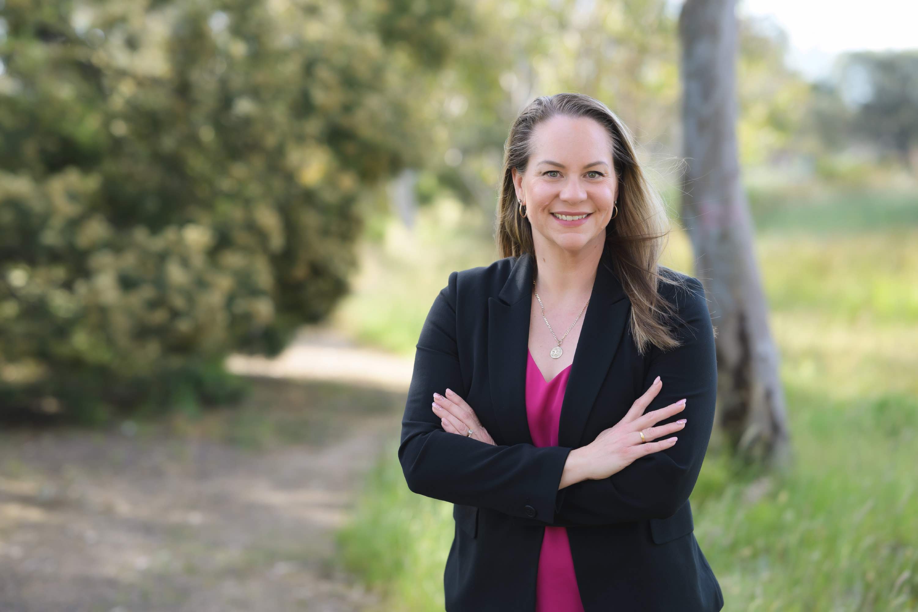Adrienne Merlo standing in nature and smiling at the camera with her arms crossed 