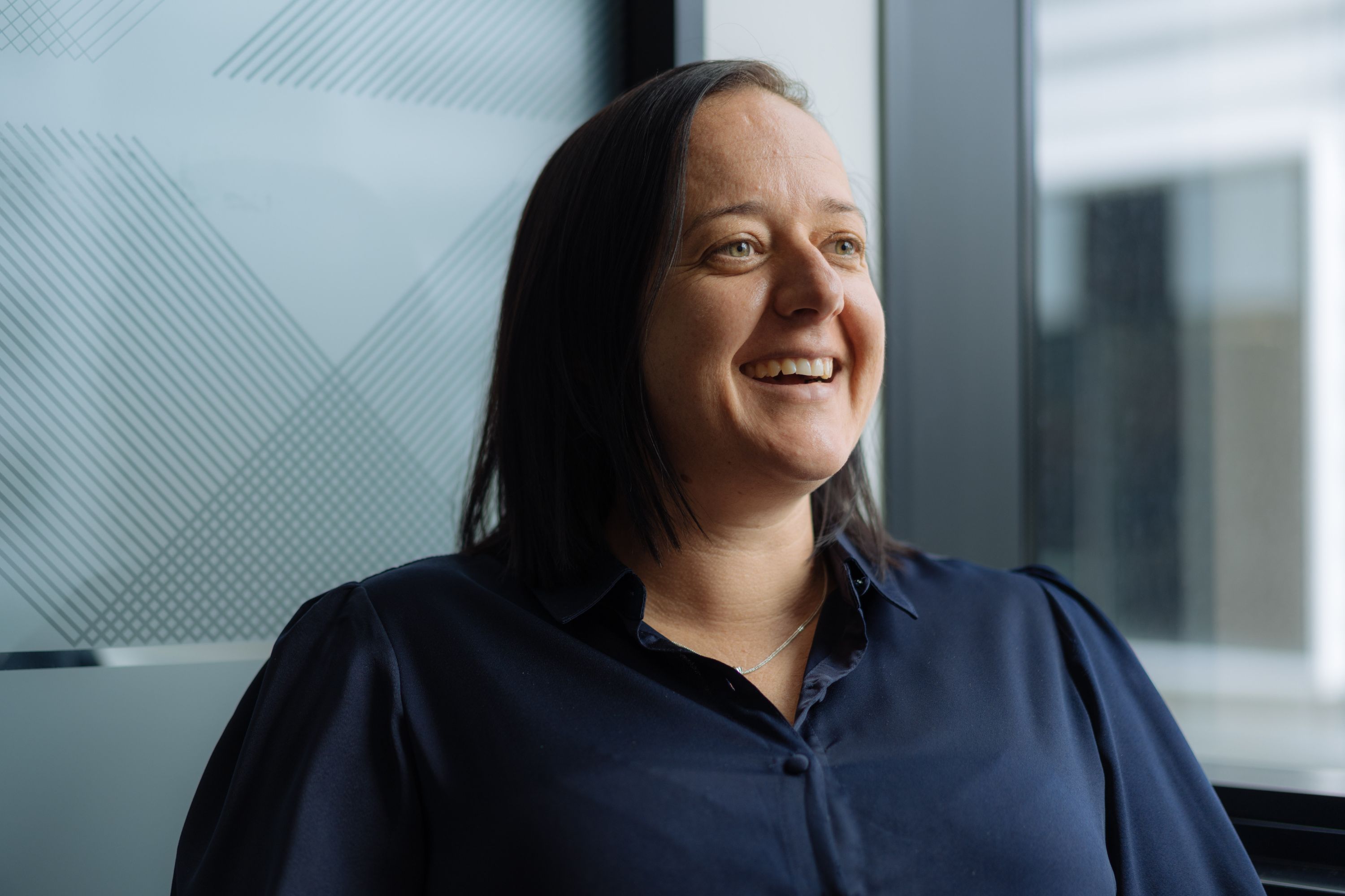 Photo of Desiree Hutcheon wearing a navy blue top smiling in front of a window