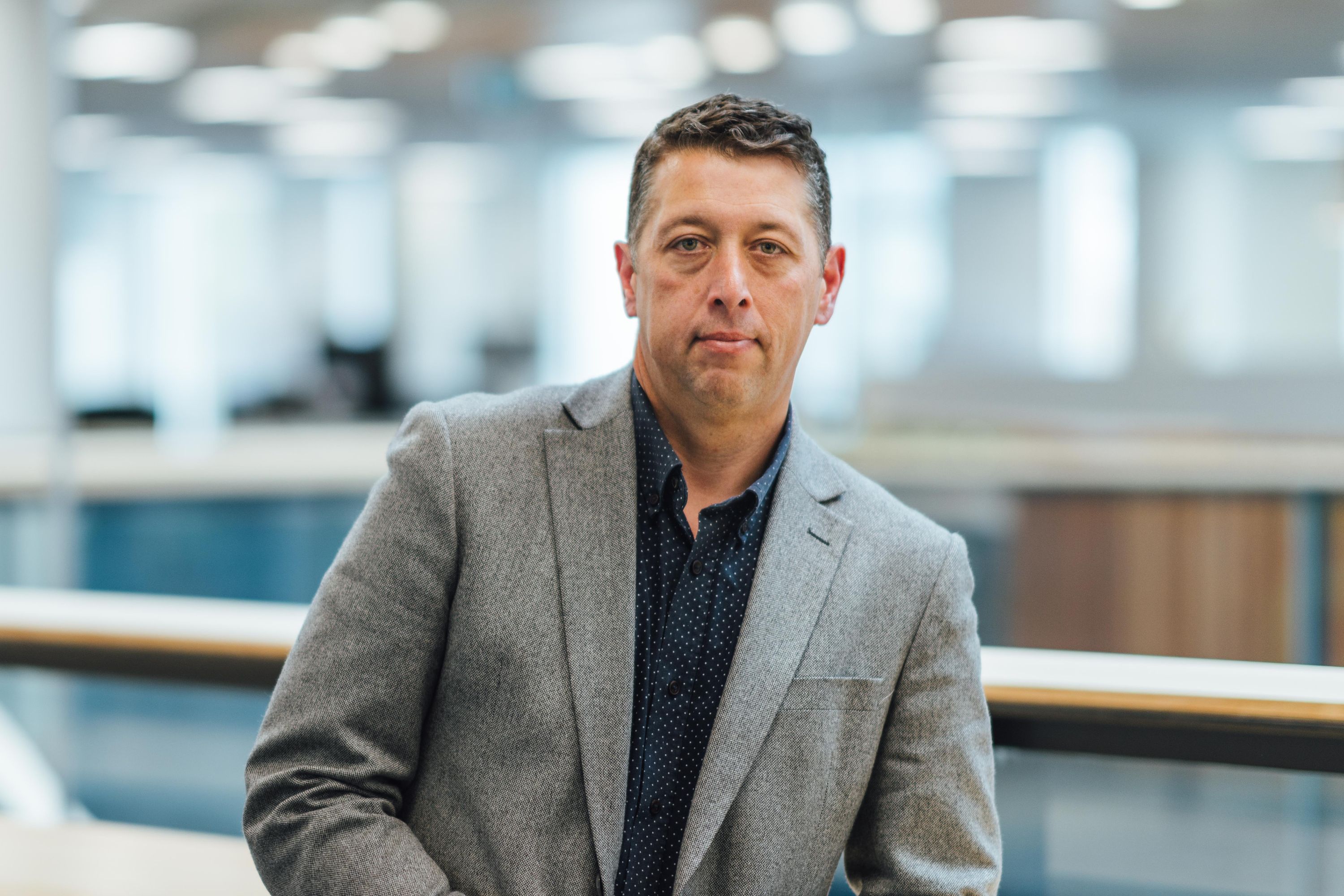 Photograph of Justin Gray wearing a grey suit jacket over a navy blue shirt