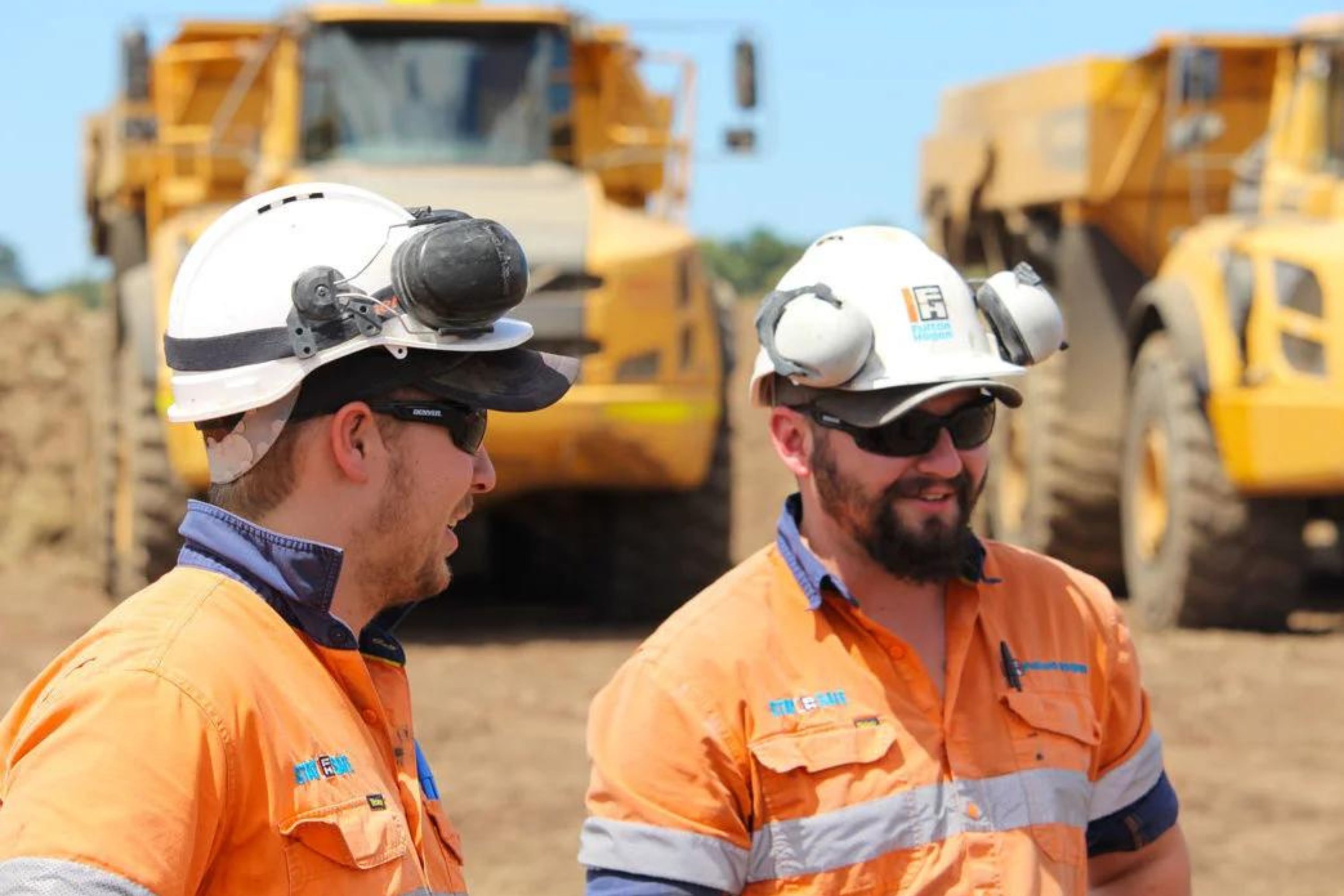 Close-up of tradies in high-vis wearing helmets in front of two trucks