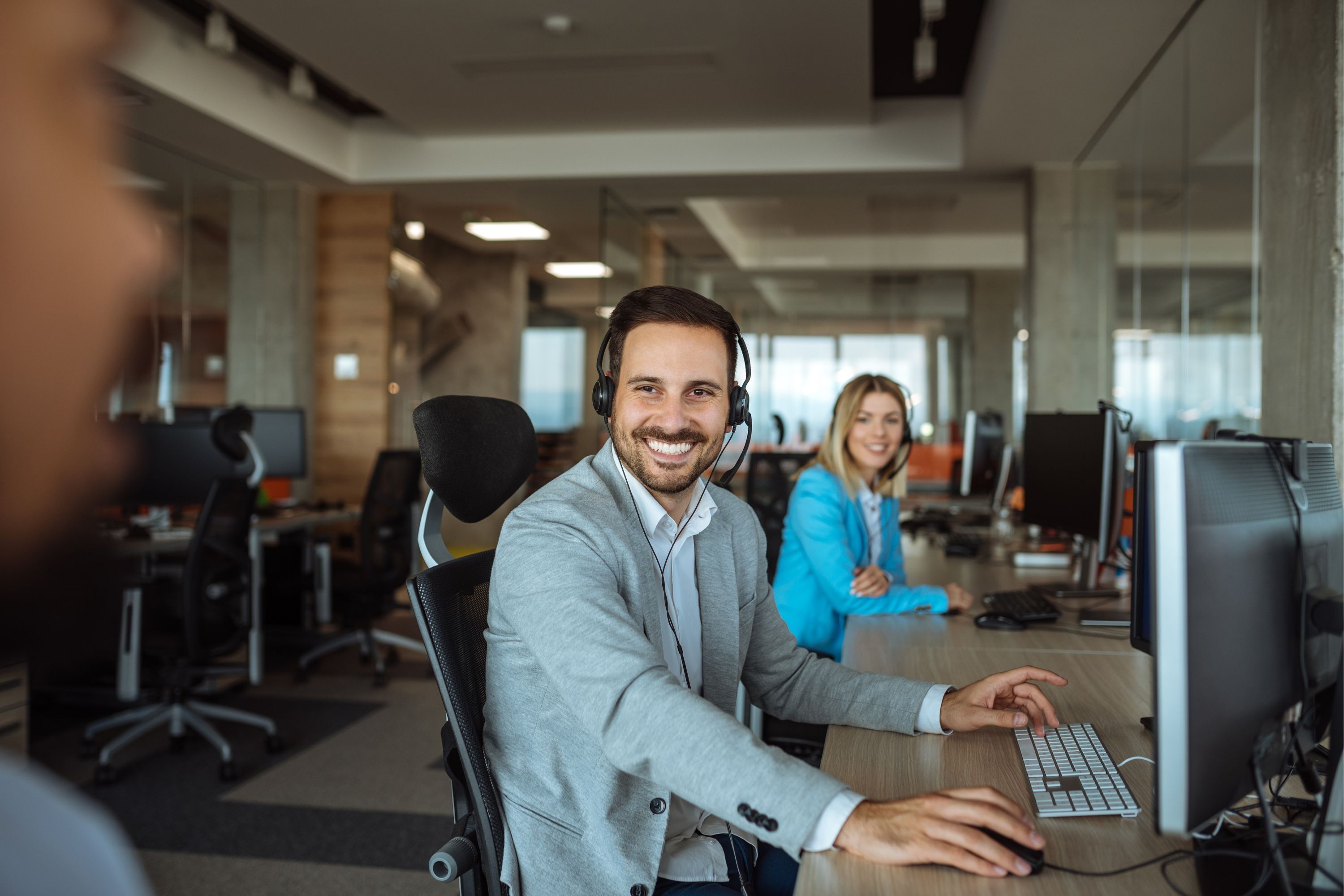 Man smiling at camera sitting at desk wearing suit and headset in office