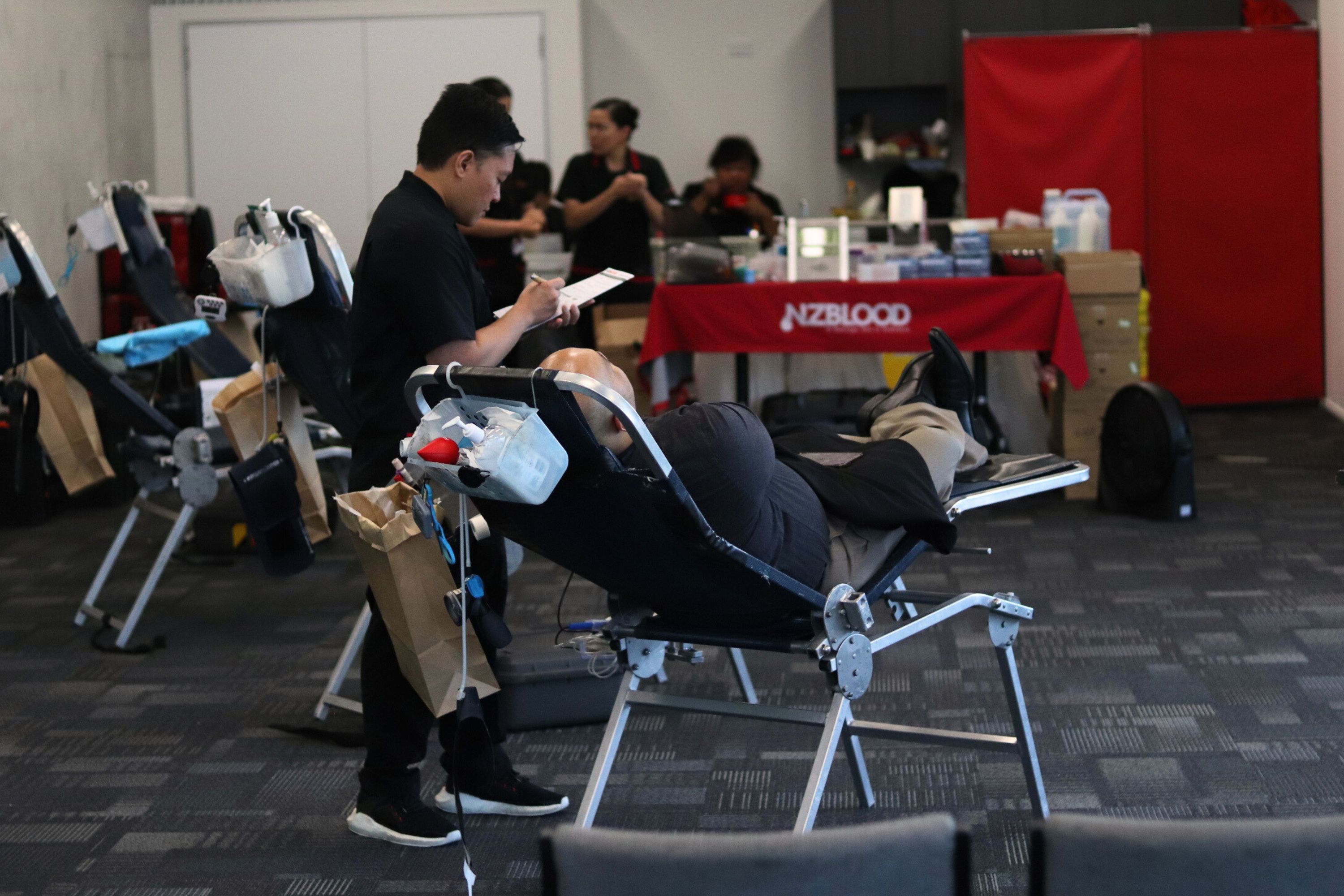 Photograph of a patient sitting in a chair having their blood pressure taken by a male nurse holding a clipboard