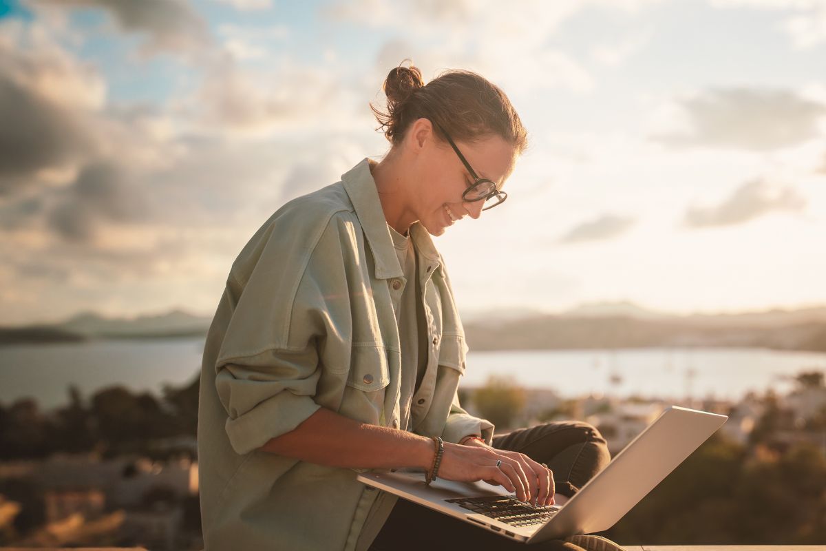 Woman smiling at computer sitting outside overlooking bay 