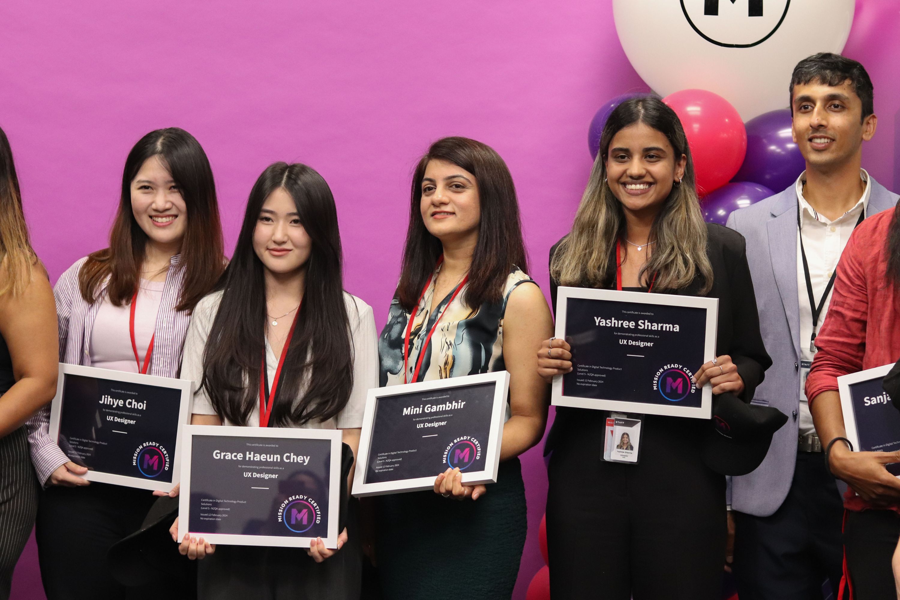 Candidates at the February 2024 Mission Ready graduation, holding graduation certificates standing against pink backdrop