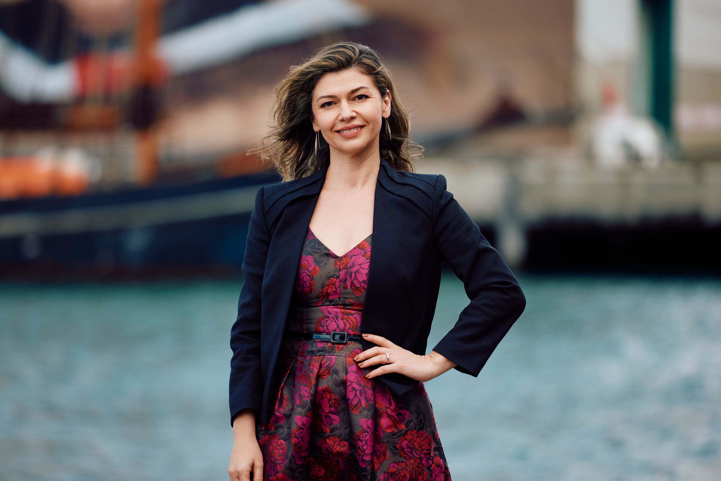 Veronika wearing a red dress and black blazer, smiling with a hand on her hip