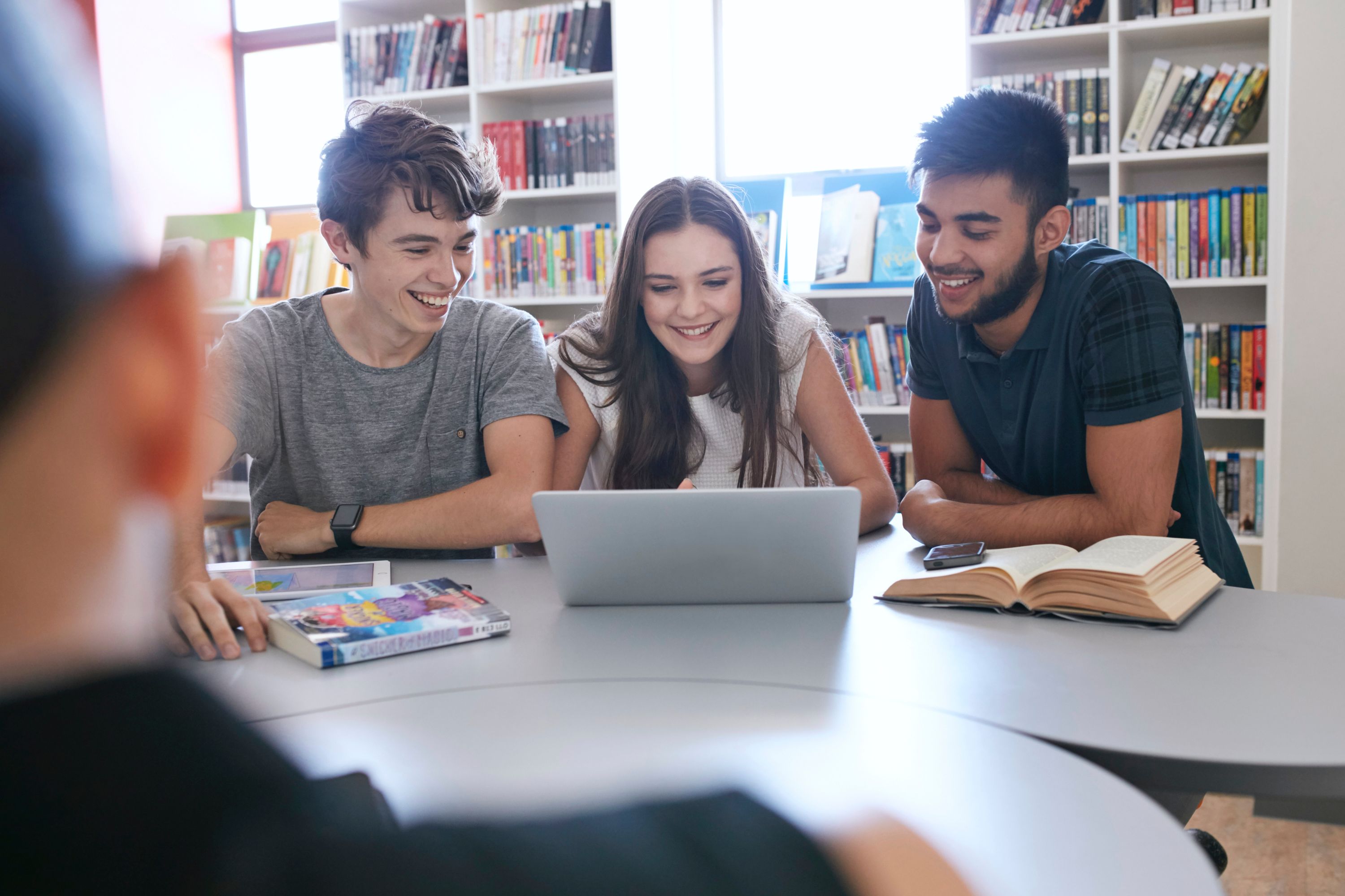 Three students in library looking at laptop and books