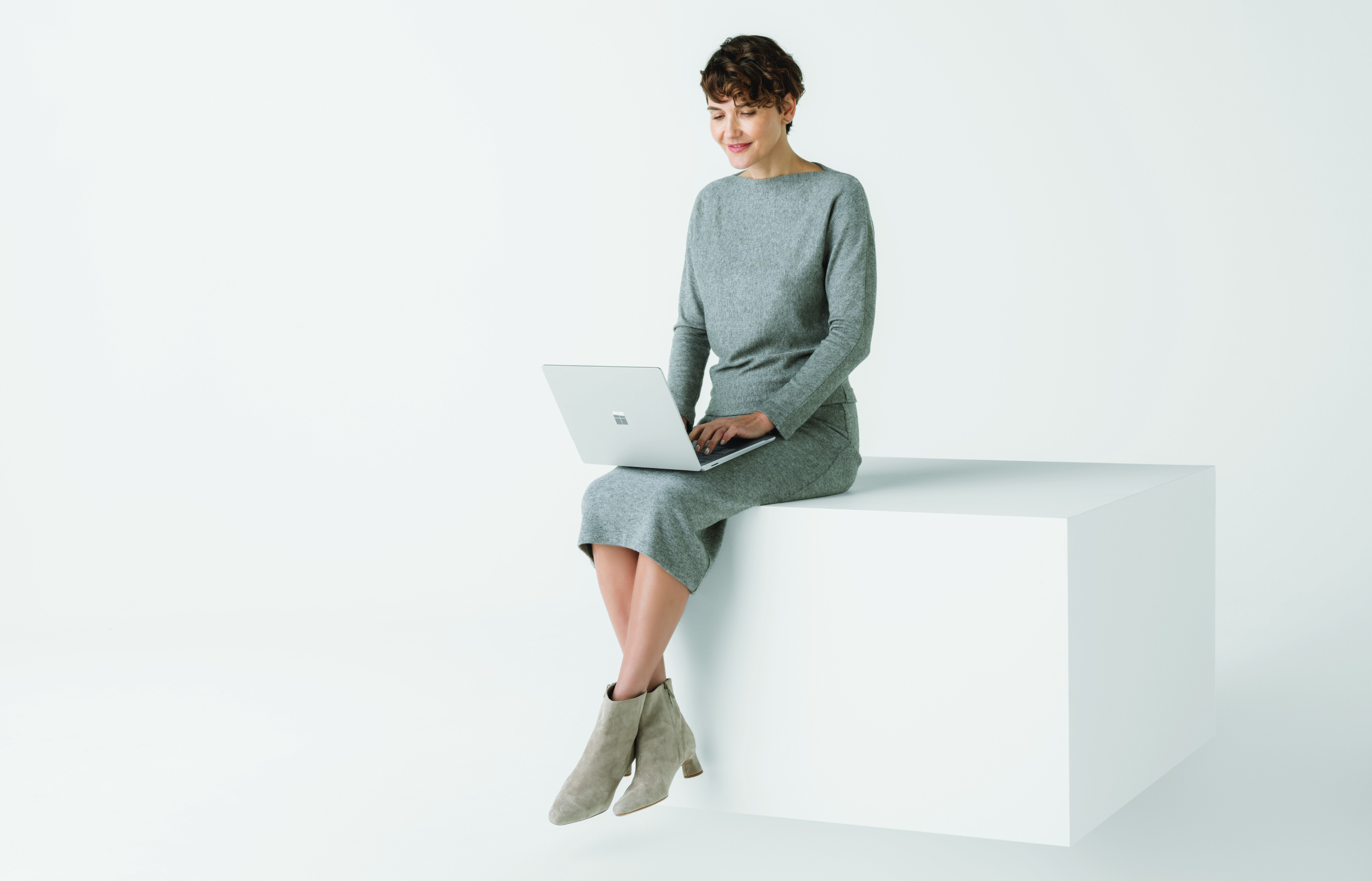 Woman sitting on white box, typing on a Windows laptop