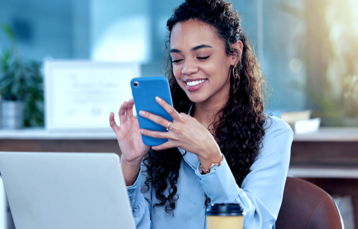 A woman wearing a sky blue coloured shirt smiling while looking at a mobile phone