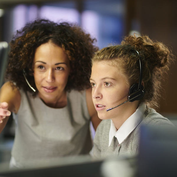 Two women with headsets working together in front of a screen